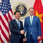 両国国旗の前で握手するベトナムのグエン・ホン・ジエン商工大臣とジェミソン・グリア米国通商代表