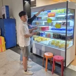 殺人の凶器を隠した空港内の飲料販売棚を確認する容疑者
