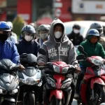 強烈な日差しを避けてバイクに乗るホーチミン市民