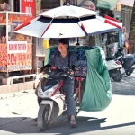 ベトナム北部の猛暑の中パラソルをさしたバイクを運転するドライバー