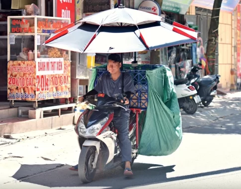 ベトナム北部の猛暑の中パラソルをさしたバイクを運転するドライバー